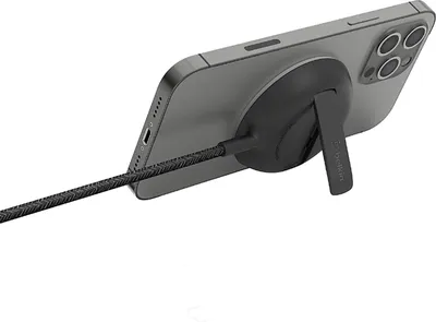 A smartphone is attached to a black charging accessory with a kickstand, and a braided USB-C cable is plugged into the phone.