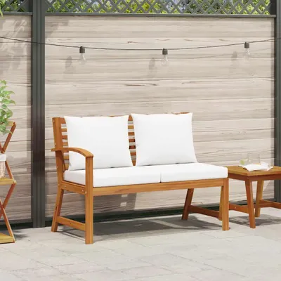 An outdoor bench with white cushions is placed on a patio next to a wooden fence and string lights.