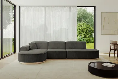 A modern living room with a large sectional sofa, large windows with sheer curtains, and a coffee table.