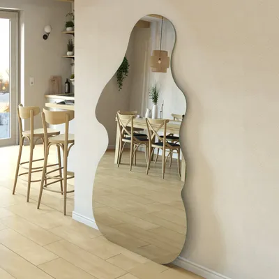 A large, irregularly shaped mirror leaning against a wall in a modern dining room and kitchen area.