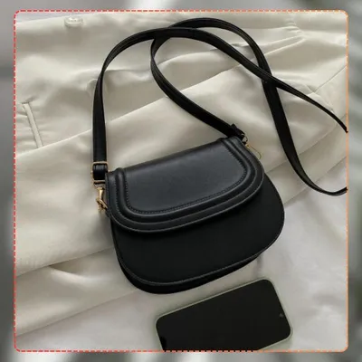 A black crossbody bag is placed on a white fabric surface, with a smartphone lying next to it.