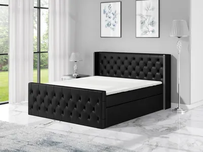 A black upholstered boxspring bed with a tufted headboard and footboard is shown in a bedroom setting.