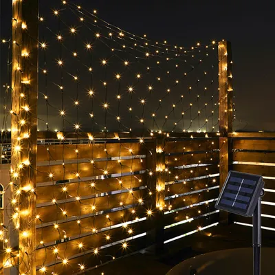 A string of warm white LED lights is draped over a wooden fence at night, with a solar panel visible in the foreground.