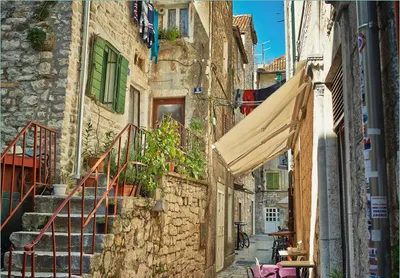 Produktbild von Wallario Fototapete Vliestapete, seidenmatte Oberfläche, einfache Verarbeitung, Größe 200 x 140 cm, Motiv Romantische Gasse in Kroatien mitten in der Stadt