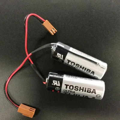 Two Toshiba lithium batteries with attached wires and connectors on a dark surface.