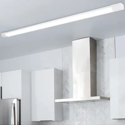 A modern kitchen with white cabinets and a stainless steel range hood, illuminated by a long, slim LED ceiling light.
