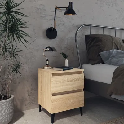 A bedside table with a lamp, book, and vase next to a bed.