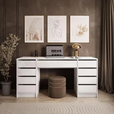 A modern home office setup with a white desk, laptop, lamp, and artwork on the wall.
