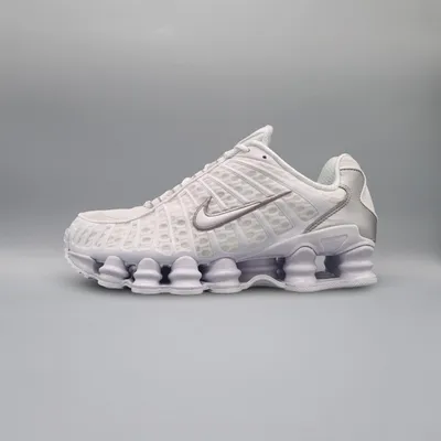 A white Nike Shox TL sneaker with silver accents is shown against a light gray background.