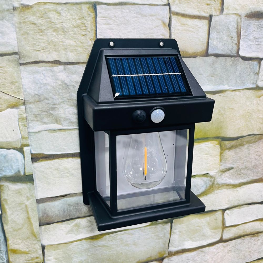 Schwarze Solar-Wandleuchte mit LED-Birne und Panel an Steinwand.