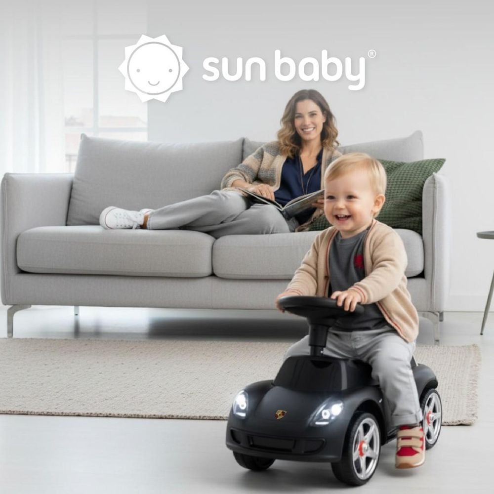 Enfant jouant avec le porteur SUN BABY dans un salon, adulte en arrière-plan.