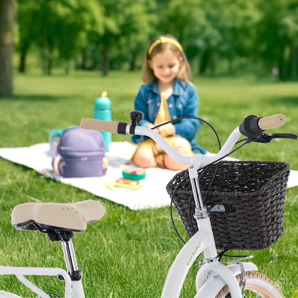 Bicicletta con cestino in primo piano, bambina seduta su una coperta da picnic sullo sfondo.