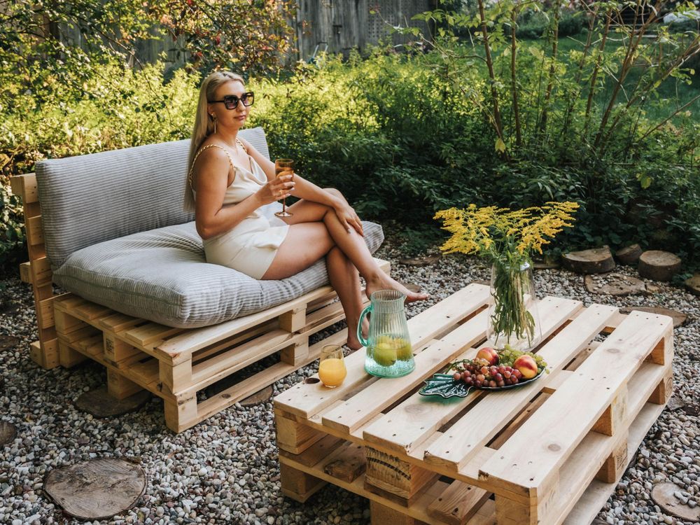 Gartenlounge mit hellgrauen Kissen auf Palettenmöbeln und sommerlicher Deko im natürlichen Umfeld.