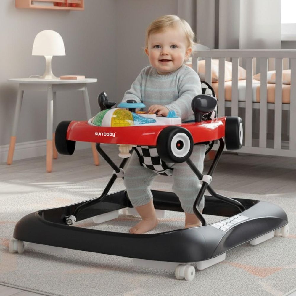 Bebé sentado en el tacatá SUN BABY en forma de coche de carreras en una habitación infantil.