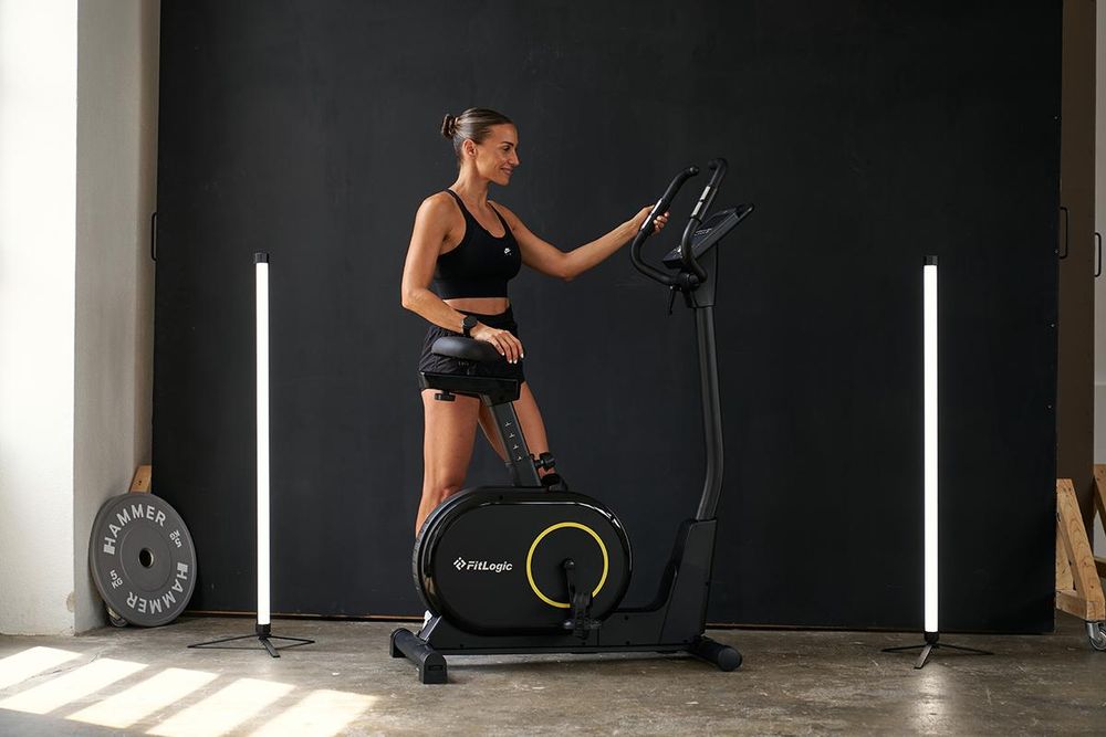 Das Bild zeigt eine Frau, die an dem Ergometer FitLogic Cardio X2 steht, eine Hand am Sattel