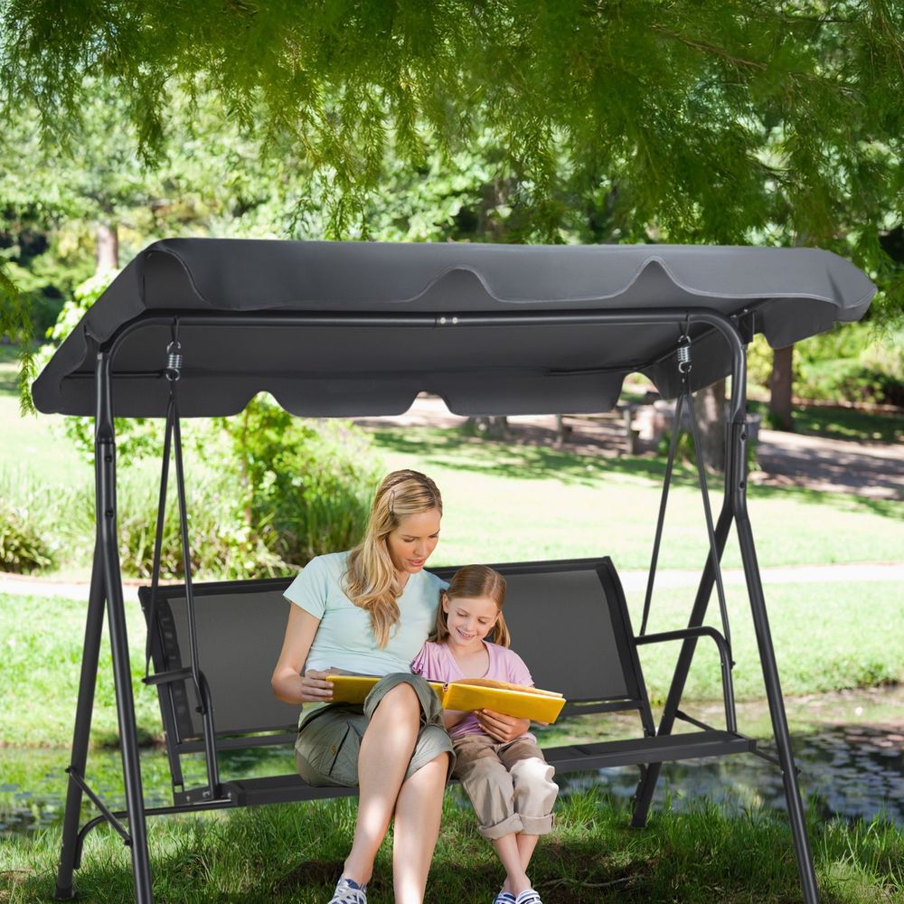 Mutter liest ihrer Tochter ein Buch auf einer grauen Gartenschaukel vor.