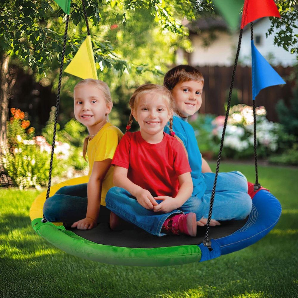Drei Kinder sitzen gemeinsam lachend auf einer bunten Nestschaukel im Garten