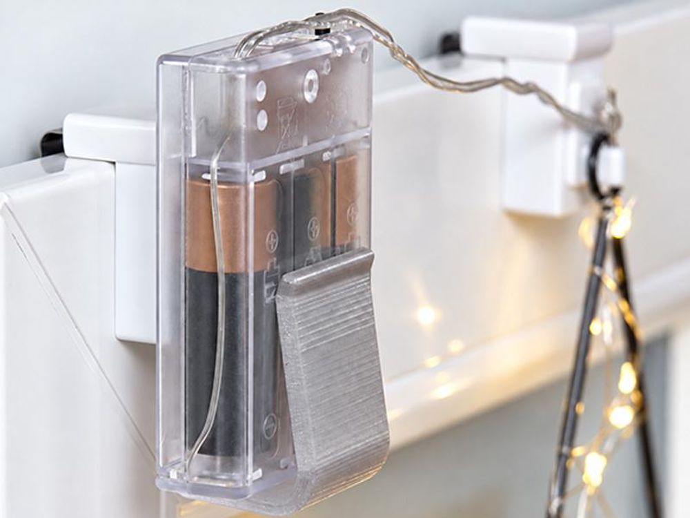 Das Bild zeigt einen klemmbaren Fensterhaken, an dem man das Batteriefach befestigen kann.