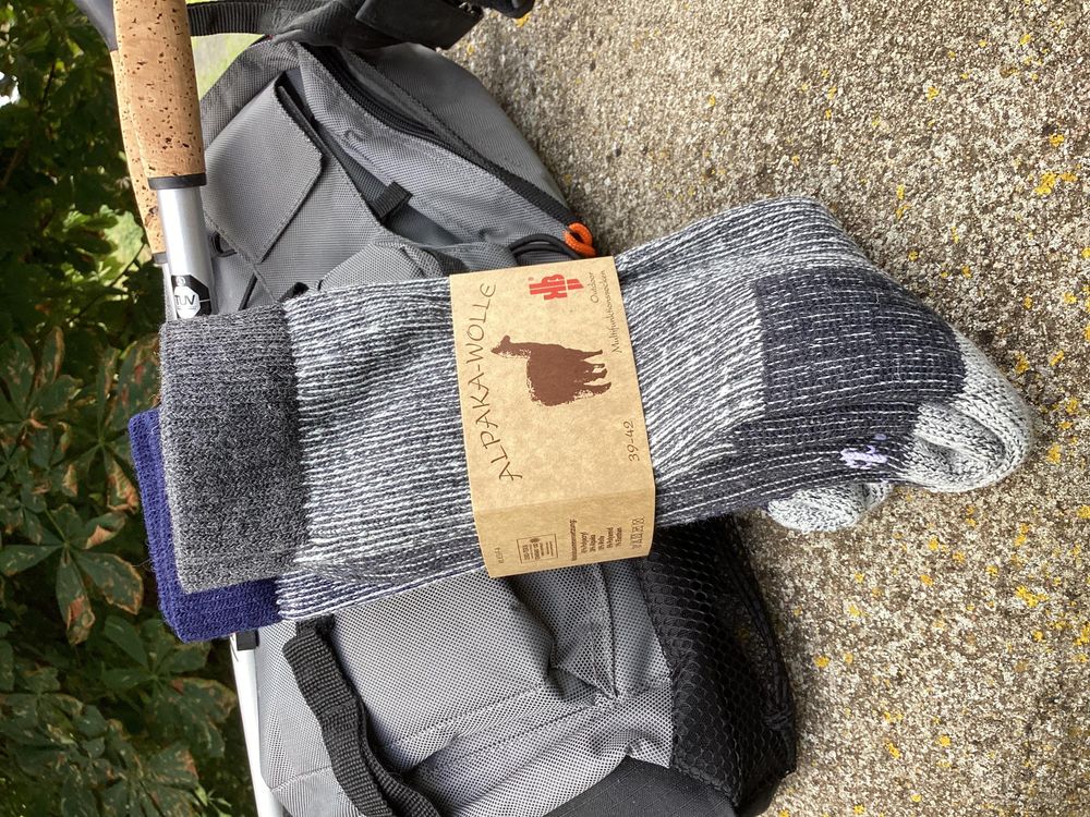 Alpaka Wander- und Arbeitssocken mit Polsterung vor Rucksack und Wanderstock.