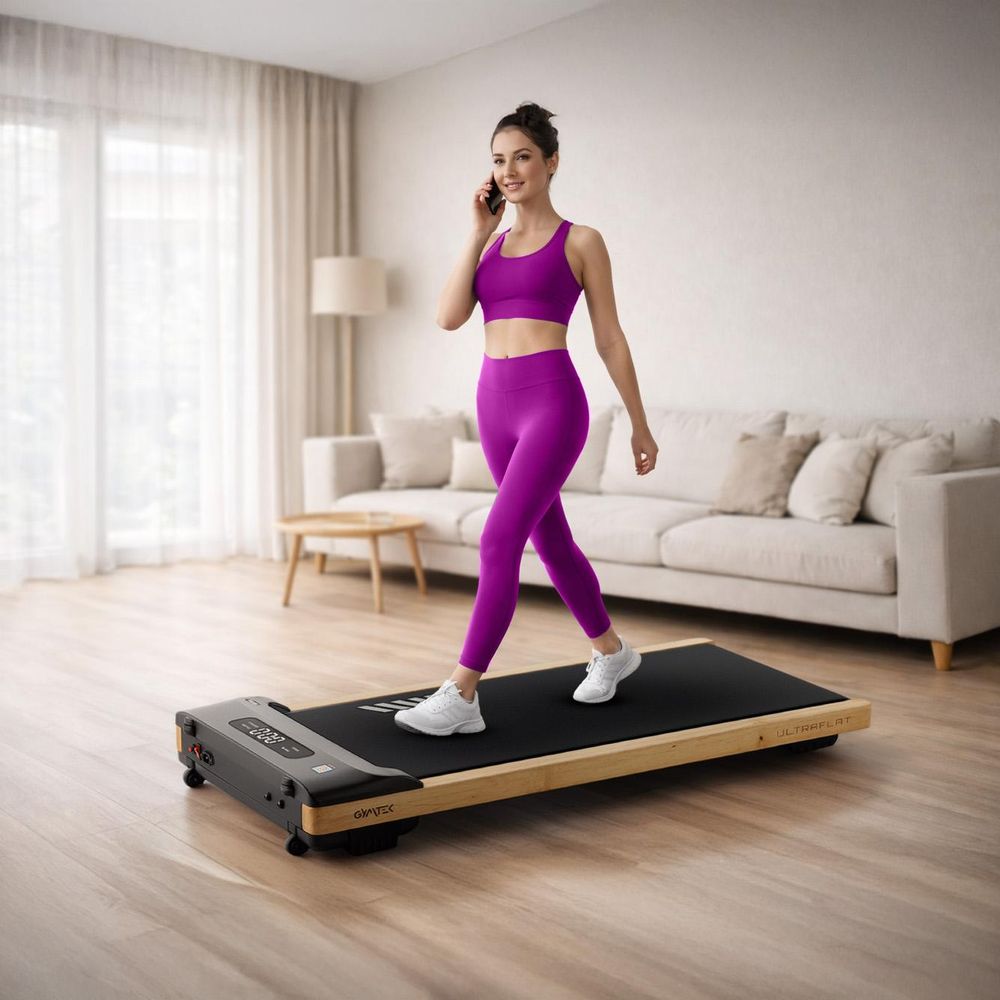 Frau telefoniert beim Gehen auf dem flachen Walking Pad zu Hause
