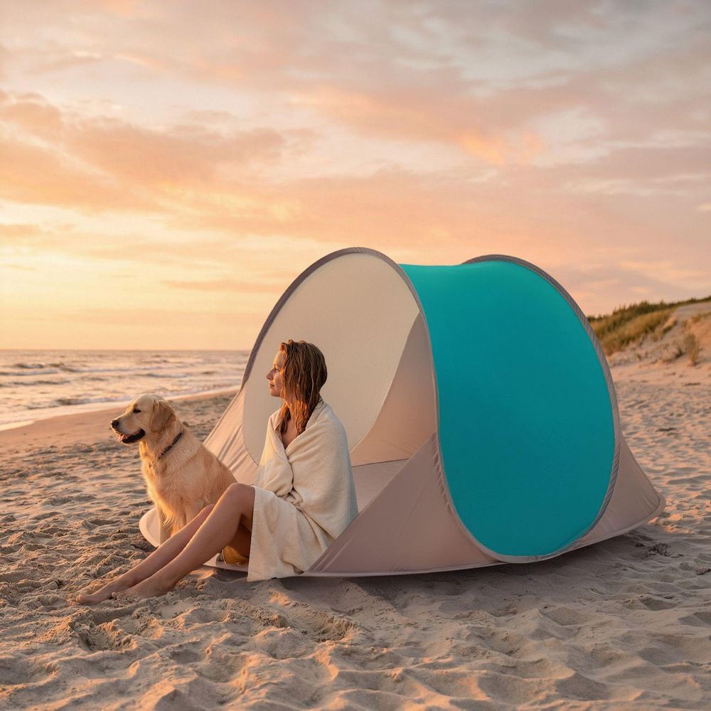 Frau mit Hund sitzt bei Sonnenuntergang am Strand vor einem Pop-up-Zelt