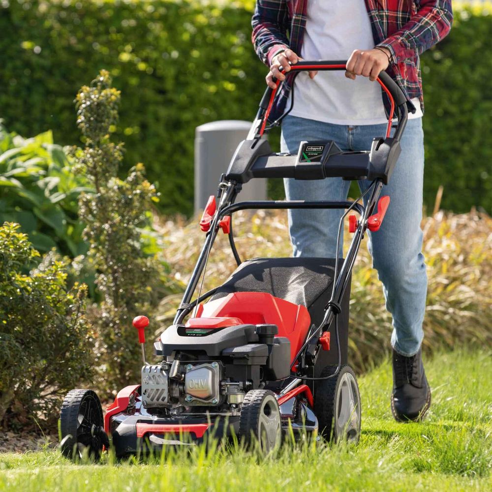 Das Bild zeigt eine Person, die den Rasenmäher durch den Garten schiebt und mäht.