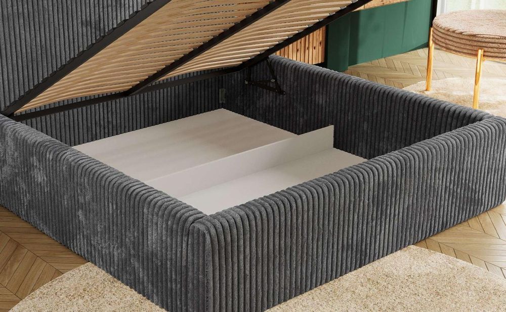 Graues Polsterbett mit geöffnetem Bettkasten und hochgeklappter Liegefläche.