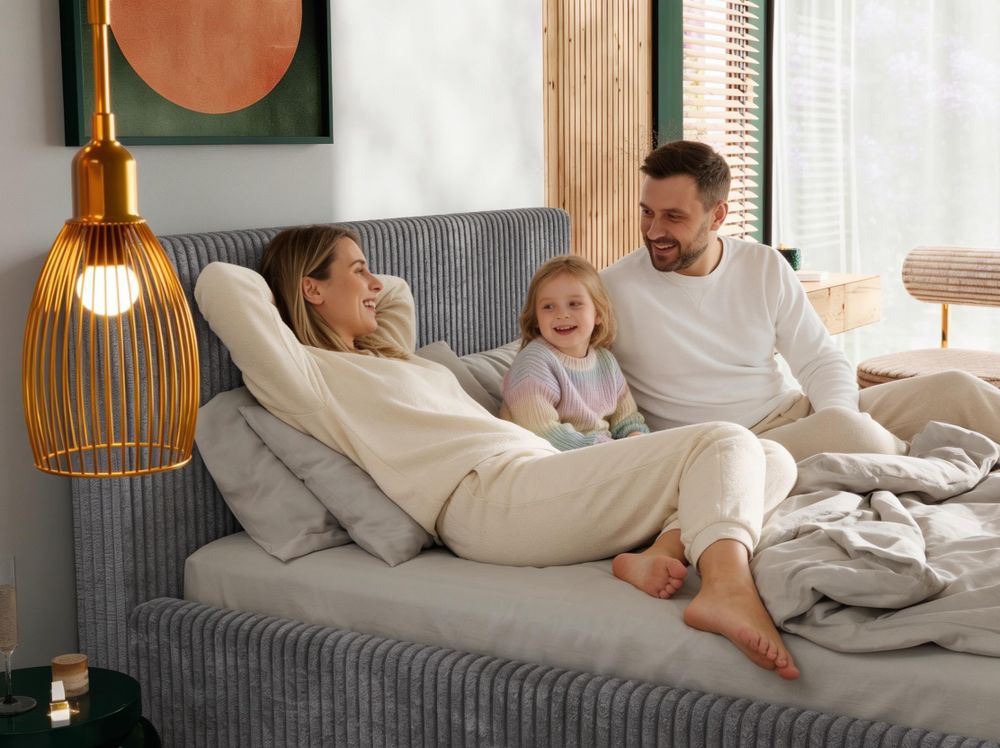 Familie spielt gemeinsam auf beigem Polsterbett im warmen Schlafzimmer.