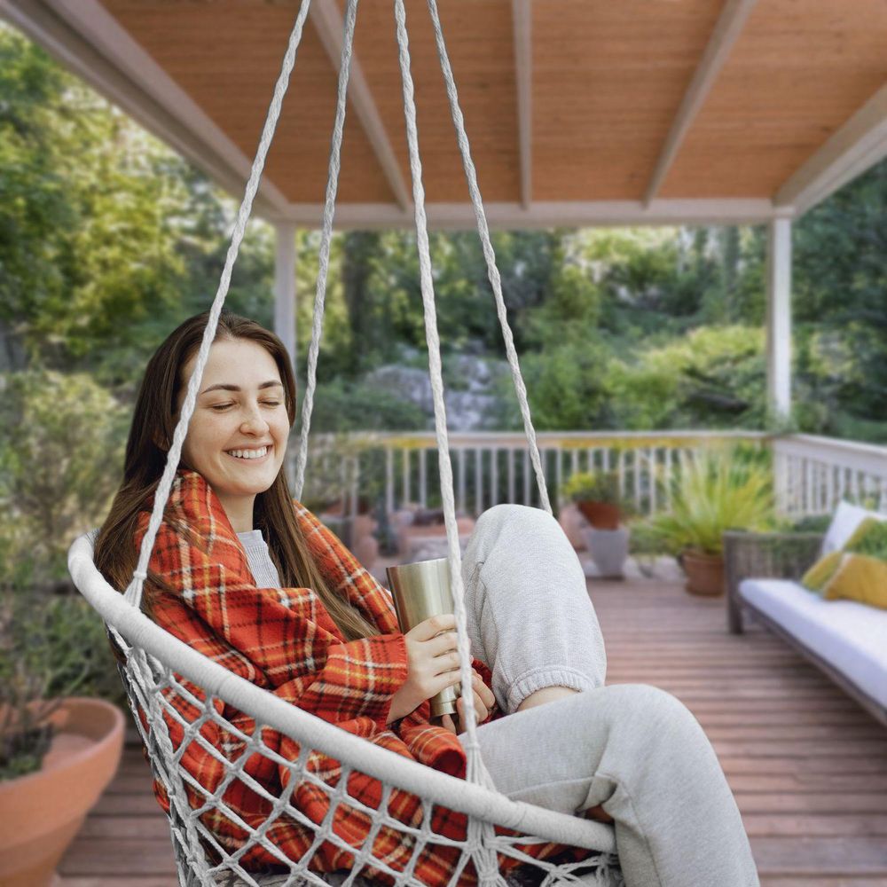 Frau in einem Hängesessel auf einer Terrasse entspannt sich mit einem Getränk