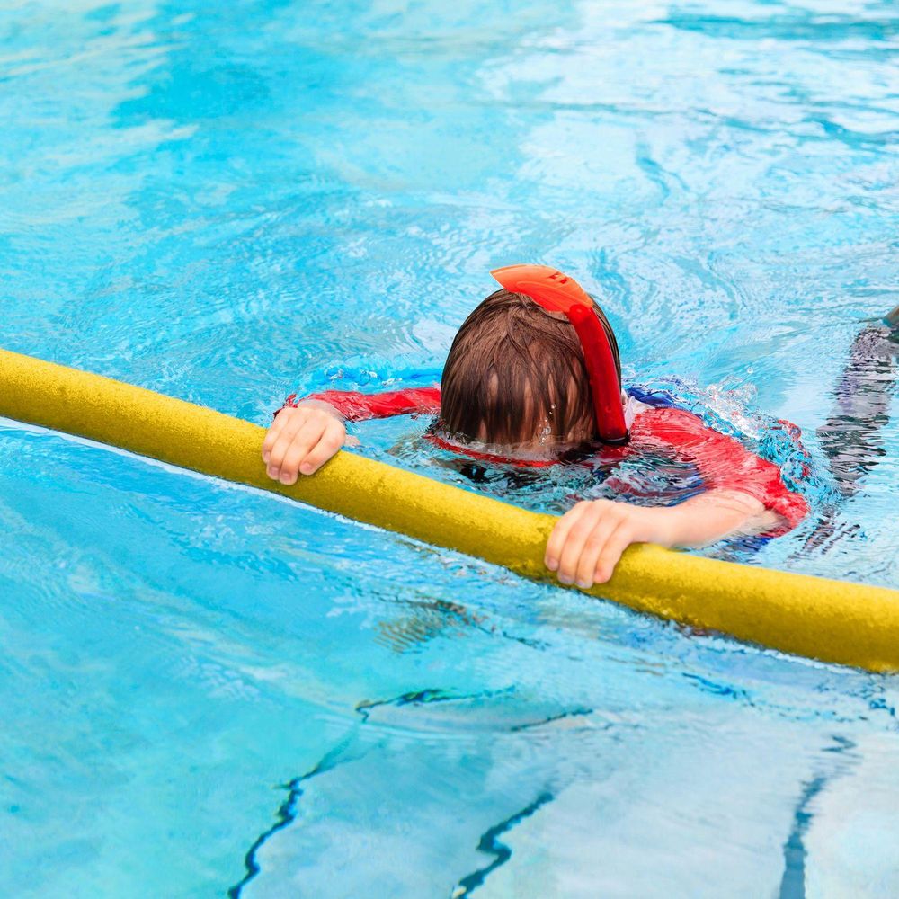 Kind im Pool mit Schnorchel, hält sich an einer gelben Schwimmnudel fes