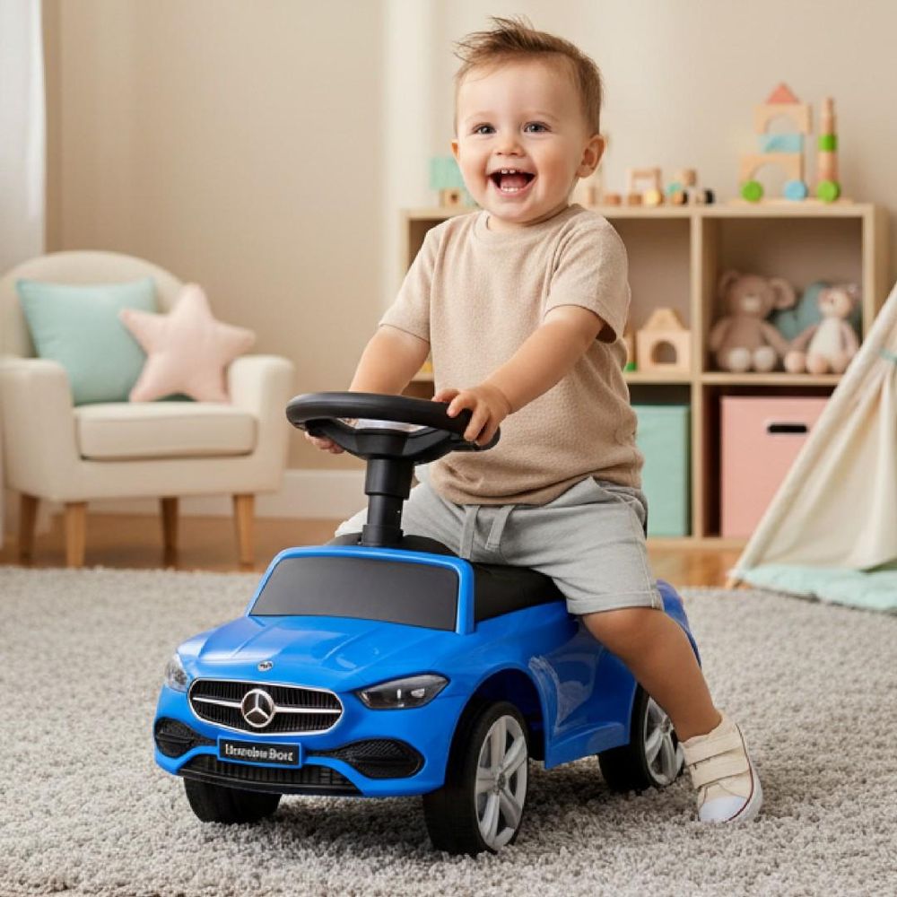 Kind zit lachend op blauwe Mercedes loopauto in kinderkamer.