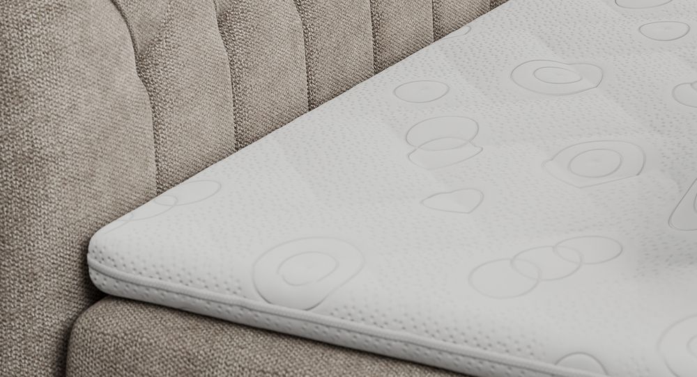 Gestepptes Kopfteil eines beige Bettes. Eine Topper-Matratze liegt auf dem Bett