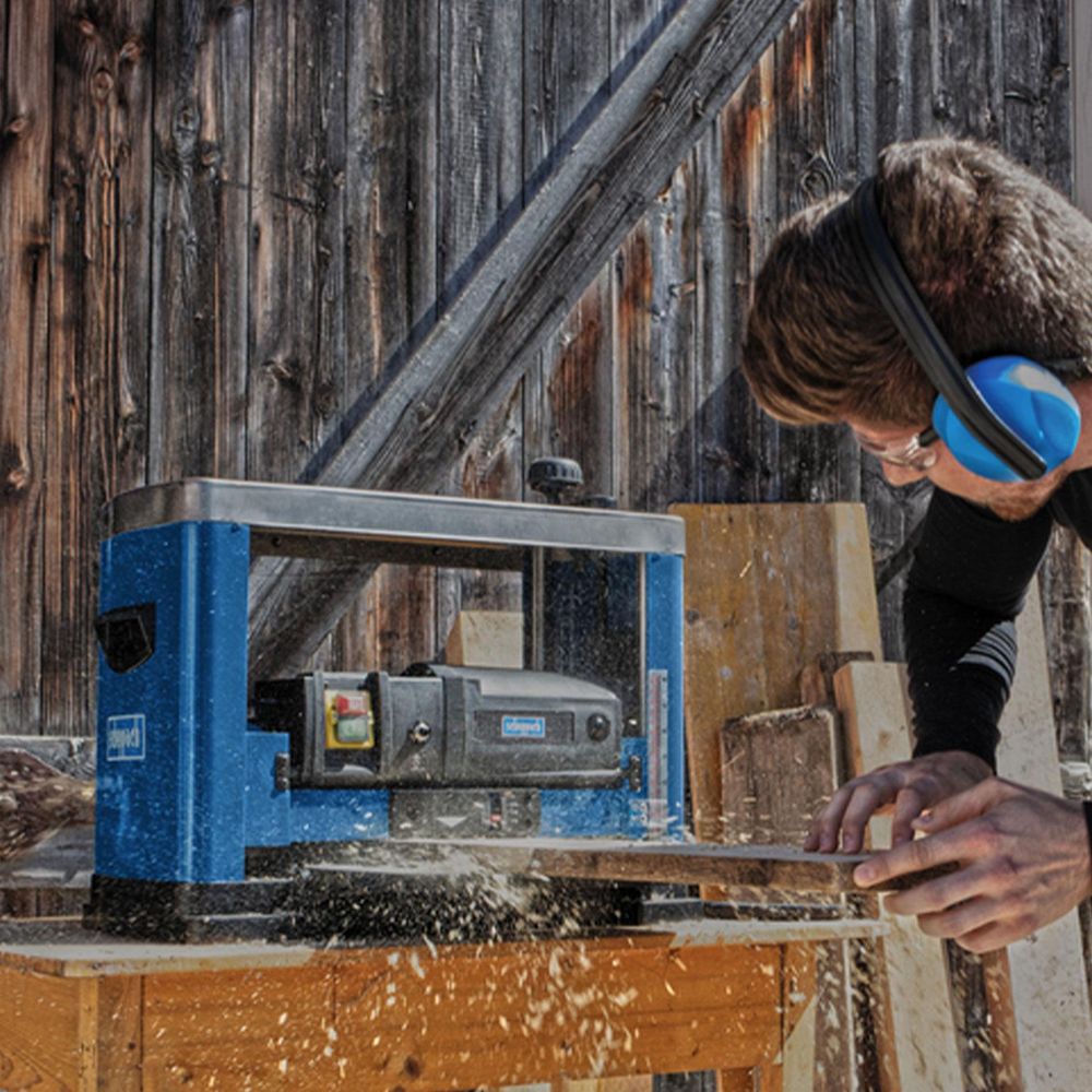 Das Bild zeigt eine Person bei der Arbeit mit Holz an der Maschine.