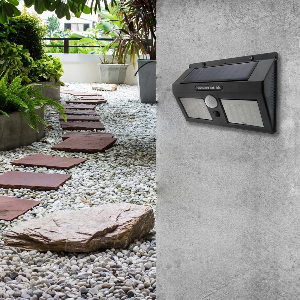 LED-Solarwandleuchte mit Bewegungssensor an grauer Gartenmauer neben Weg mit roten Trittplatten.