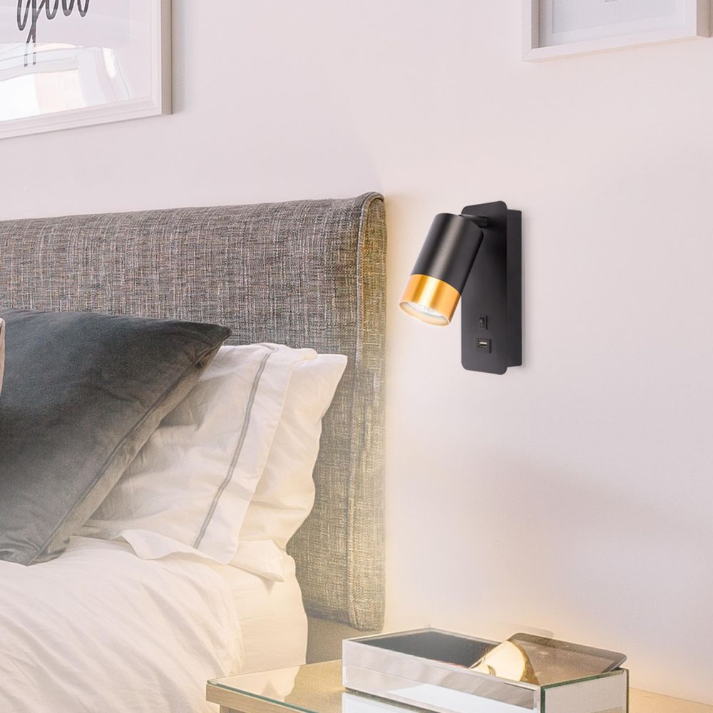 Schwarze LED-Wandleuchte mit Goldakzent und USB-Anschluss montiert neben einem gepolsterten Bett.