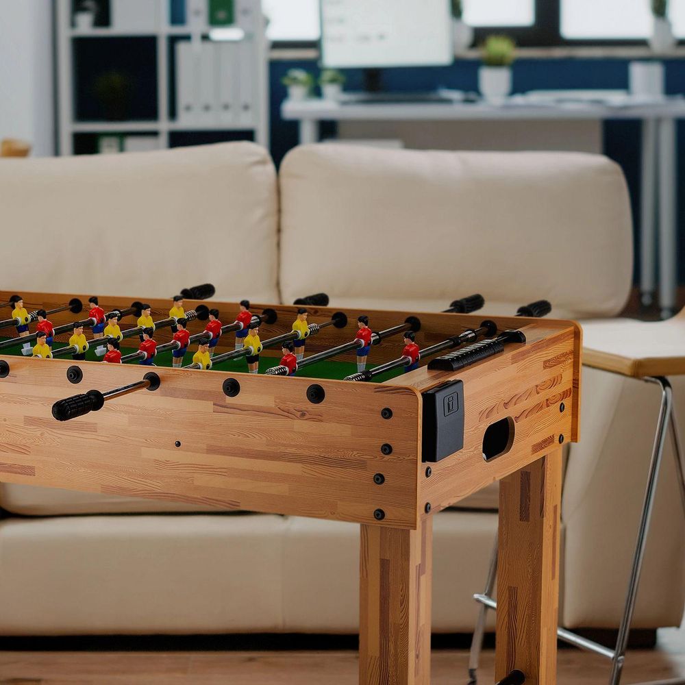 Foosballtisch aus hellem Holz mit Blick auf ein Wohnzimmer/Büro mit weißem Sofa