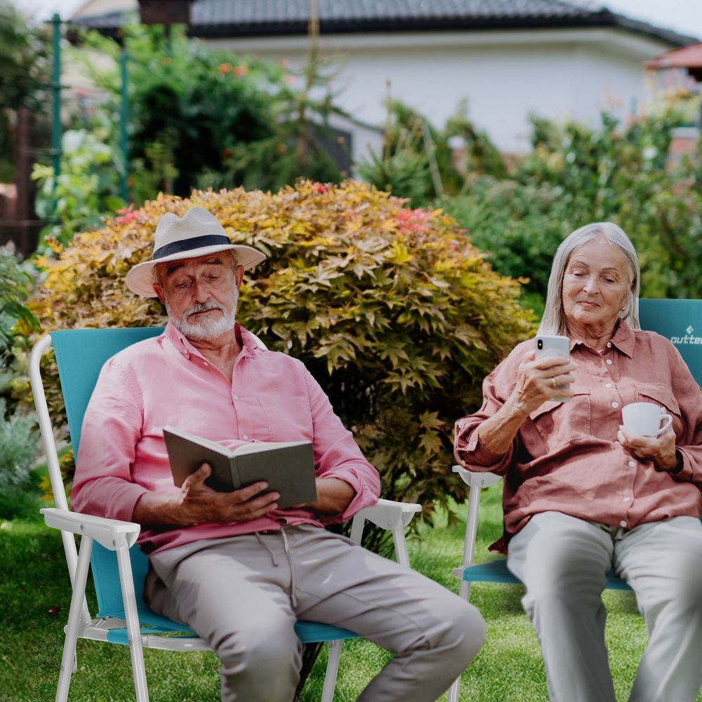 Entspanntes Seniorenpaar mit Buch und Tasse auf türkisfarbenen Liegestühlen im Garten.