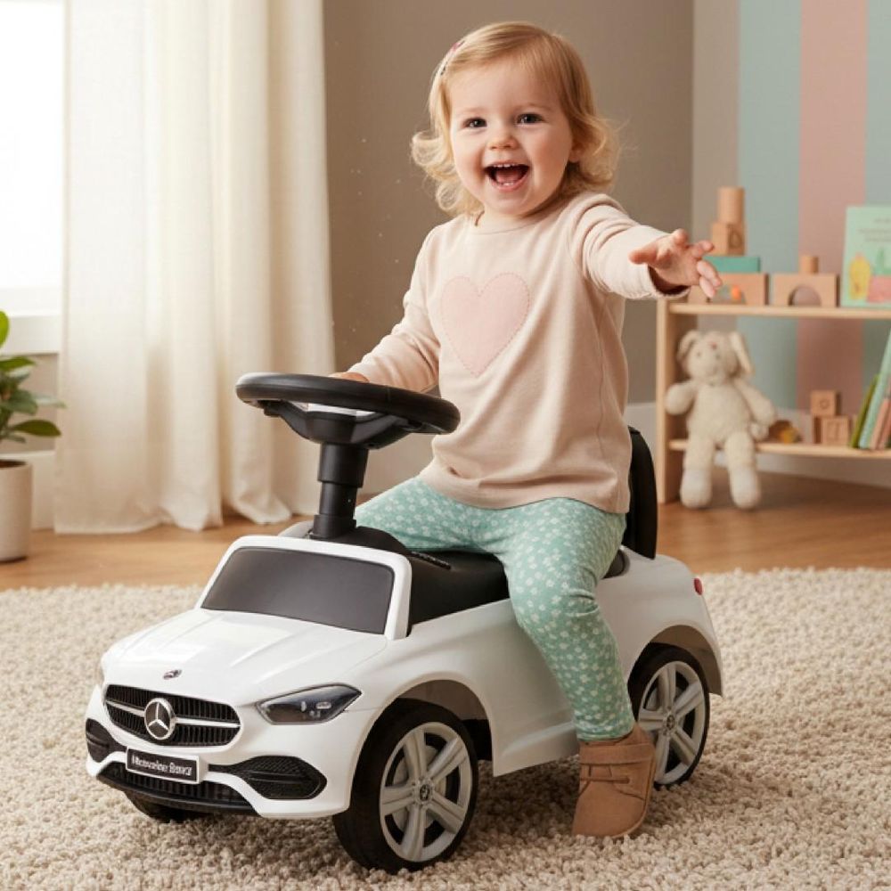 Kind zit lachend op de Sun Baby loopauto Mercedes C-Class in een kinderkamer.