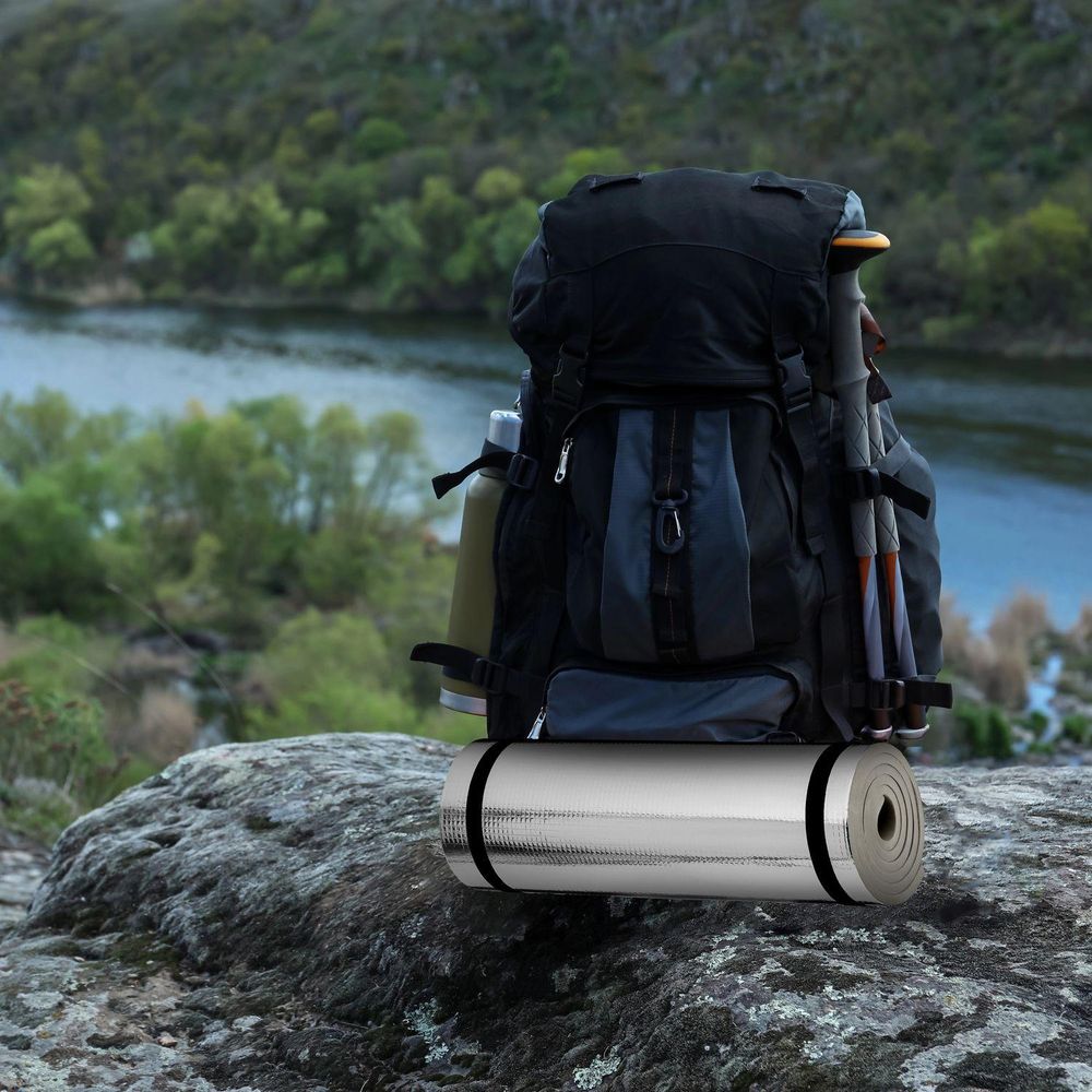 Gerollte, silberne Isomatte an Rucksack, bereit für Wanderungen in der Natur