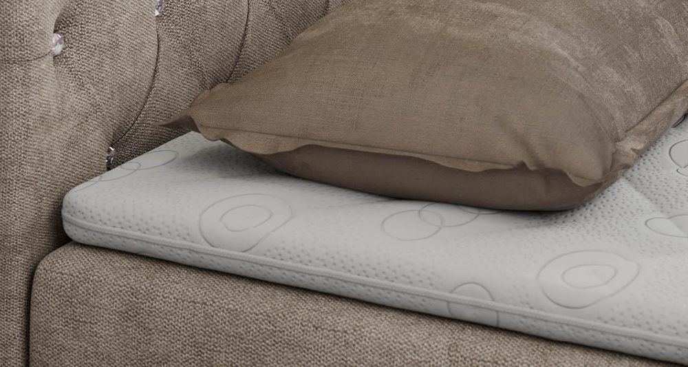 Gestepptes Kopfteil eines beige Bettes. Eine Topper-Matratze liegt auf dem Bett