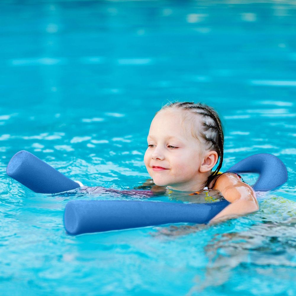 Lächelndes Mädchen im Pool mit blauer Schwimmnudel, lernt schwimmen
