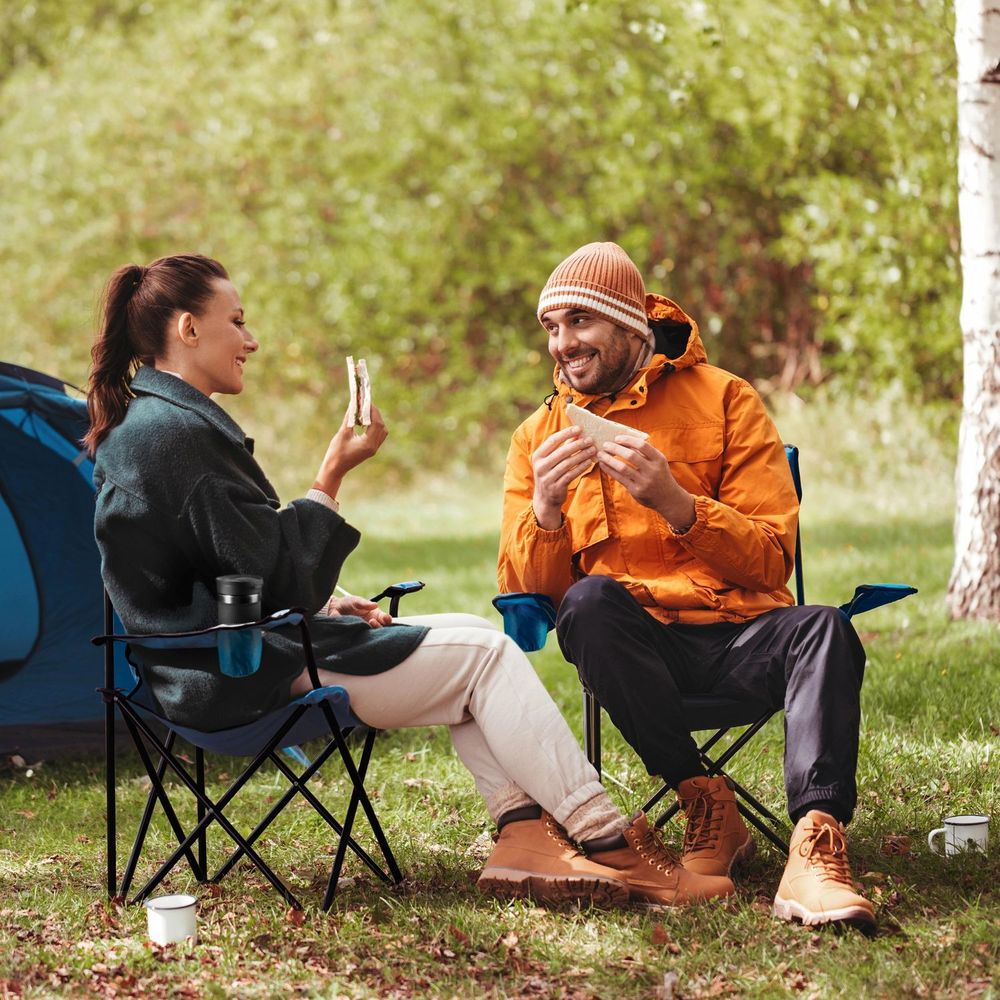 Zwei Personen sitzen auf blauen Campingstühlen vor einem Zelt.