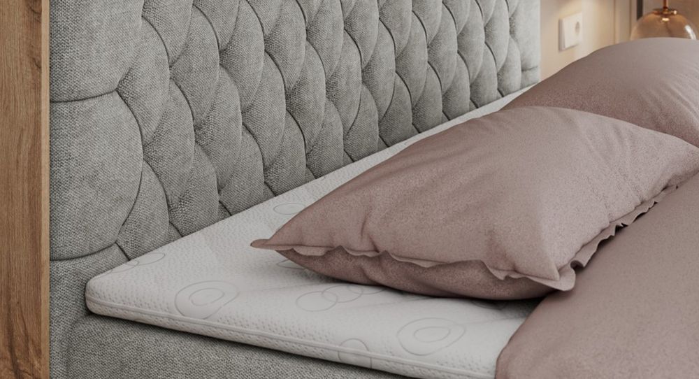 Gestepptes Kopfteil eines grau Bettes. Eine Topper-Matratze liegt auf dem Bett