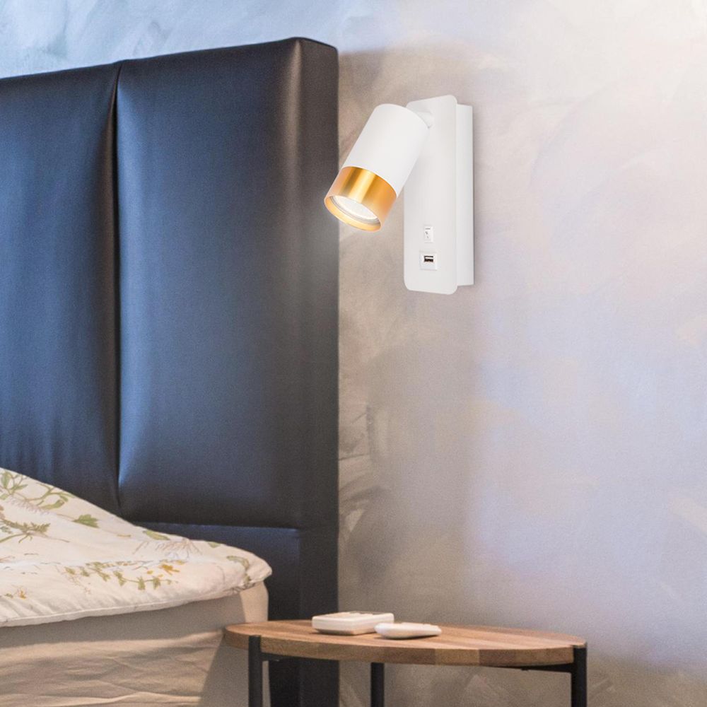 LED-Wandleuchte mit USB-Anschluss und Goldakzent über Nachttisch und Bett mit schwarzem Kopfteil.