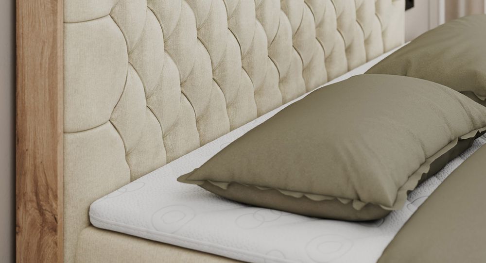 Gestepptes Kopfteil eines beige Bettes. Eine Topper-Matratze liegt auf dem Bett