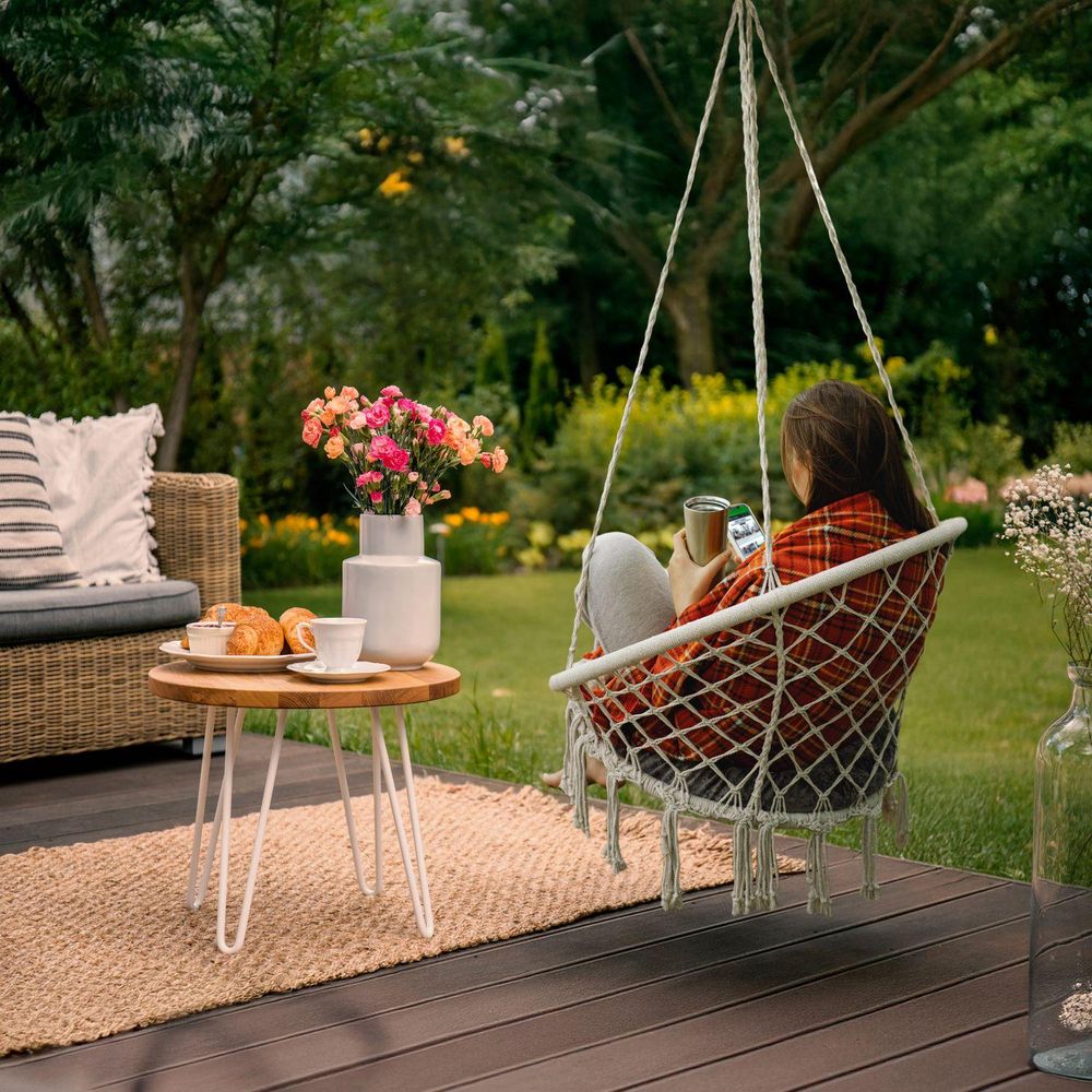 Frau in einem Hängesessel im Garten, trinkt Kaffee auf einer Holzterrasse