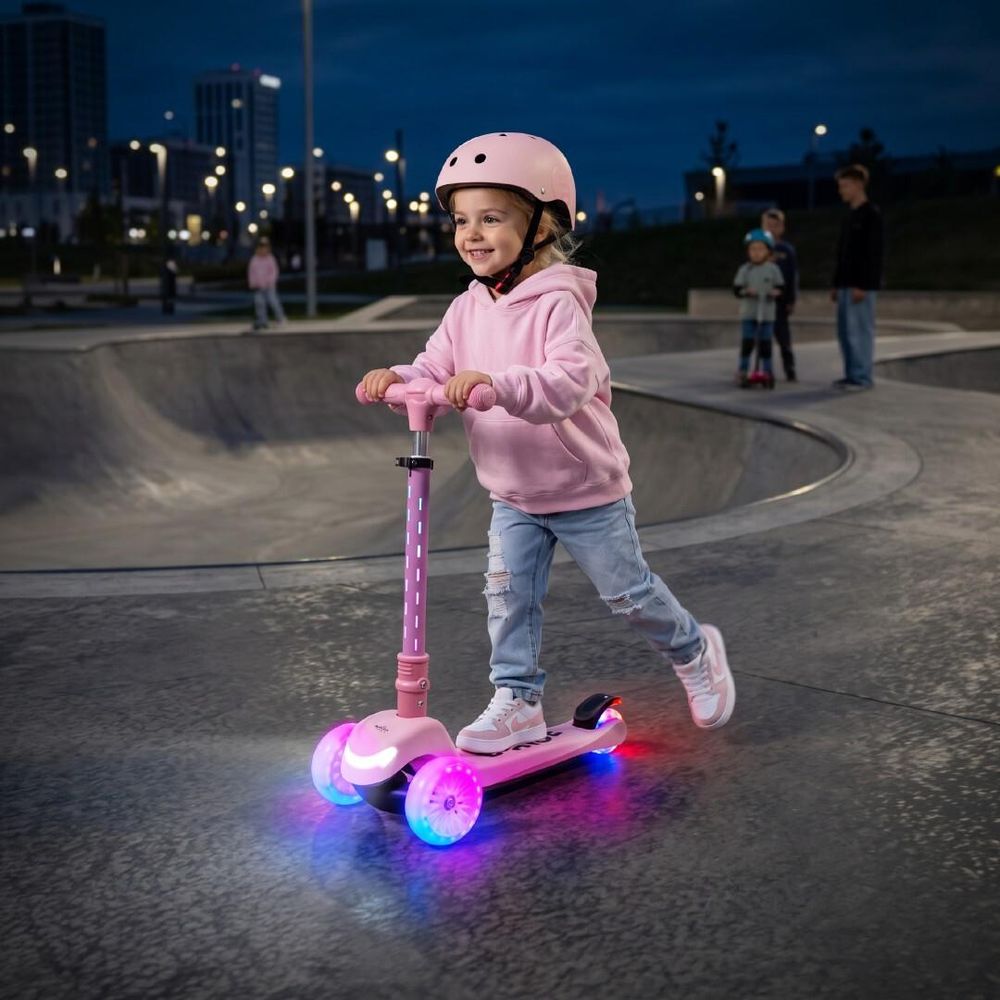 Niña montando el patinete SUN BABY LUMI RIDE en un parque al anochecer.