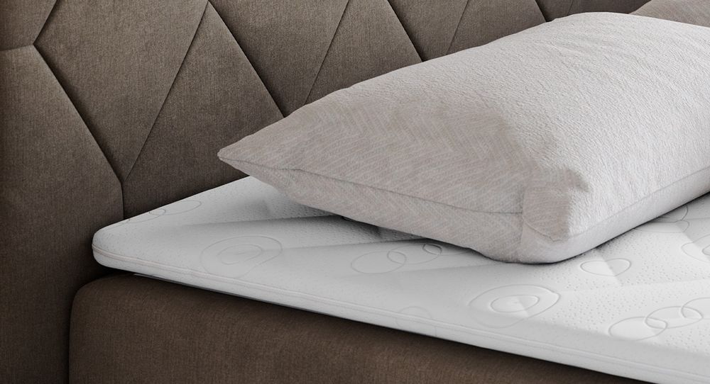 Gestepptes Kopfteil eines grau Bettes. Eine Topper-Matratze liegt auf dem Bett