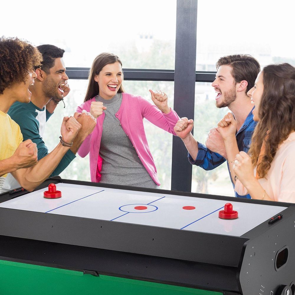 Gruppe lachender Freunde spielt Airhockey und feiert einen Punkt
