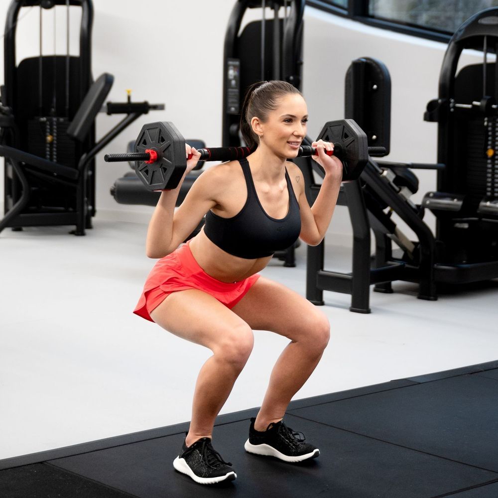 Frau macht Kniebeugen mit Hantel im Fitnessstudio.